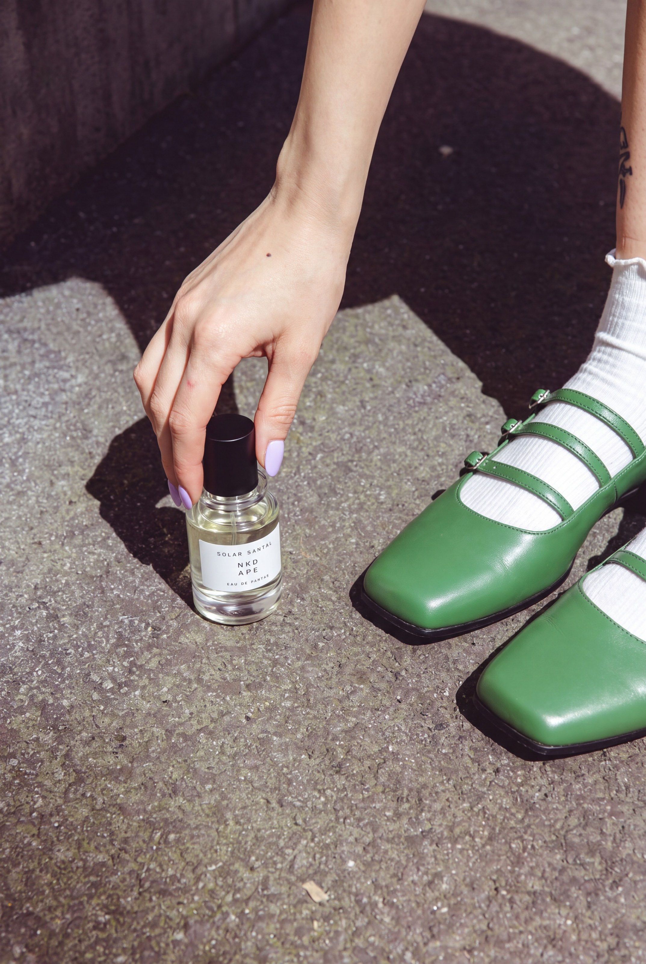 NKD APE fragrance held beside bright green shoes.